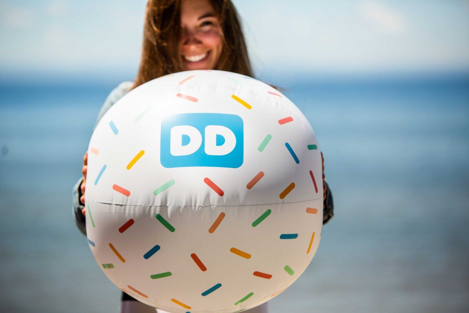 Smiling woman outside holding a large beachball with Dunkin Donuts logo